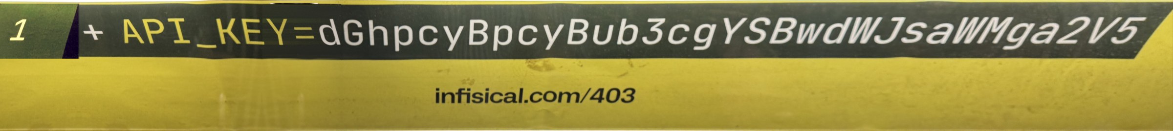 The ad itself, straightened and cleaned up from my two photos: a yellow strip with a green gutter marked 1, a dark band reading plus API_KEY equals dGhpcyBpcyBub3cgYSBwdWJsaWMga2V5, and infisical.com/403 beneath it.
